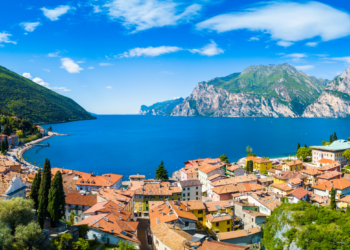 Złociste światło zachodzącego słońca odbija się w spokojnych wodach Jeziora Garda, z malowniczym Limone Sul Garda w tle.