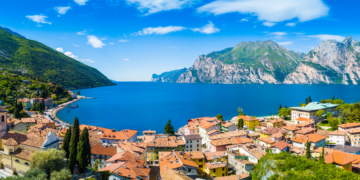 Złociste światło zachodzącego słońca odbija się w spokojnych wodach Jeziora Garda, z malowniczym Limone Sul Garda w tle.